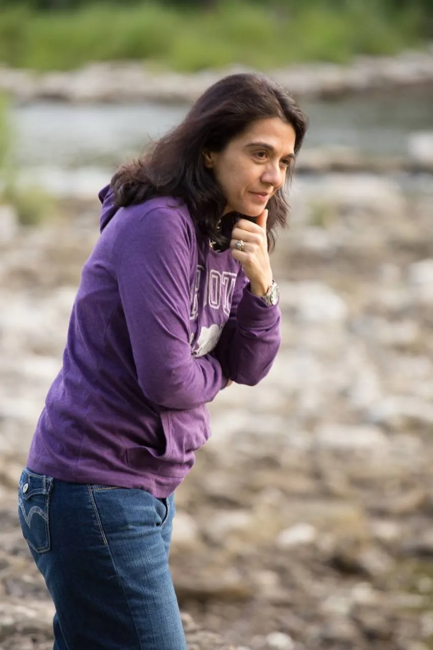 Mary Bondi in a purple hoodie, smiling thoughtfully by a river