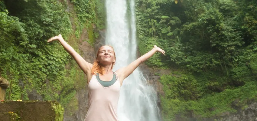 Woman with arms raised in front of a waterfall, feeling free